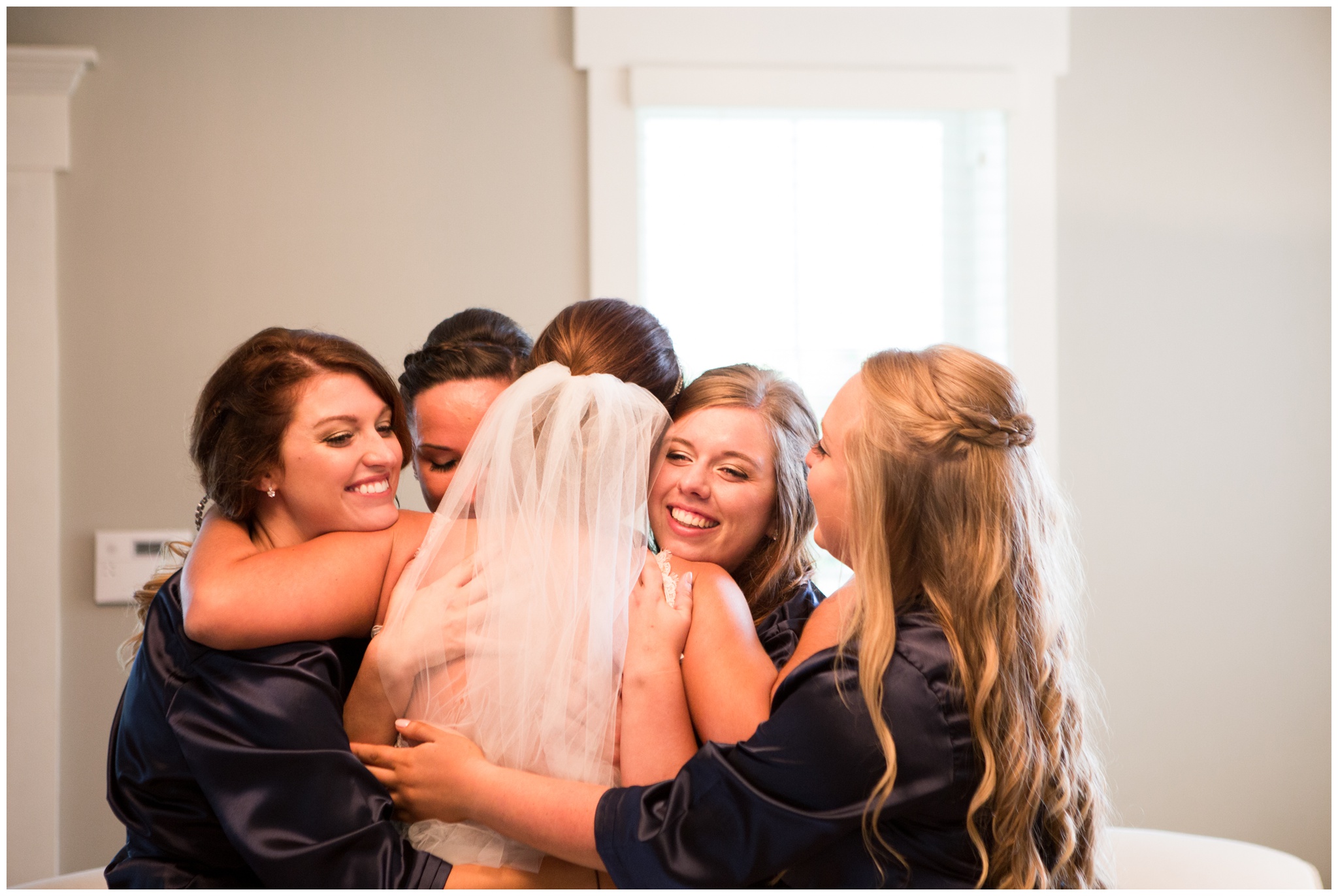 bridesmaids hug bride in wedding dress the Lodge at River Valley Farm in Yorktown Indiana
