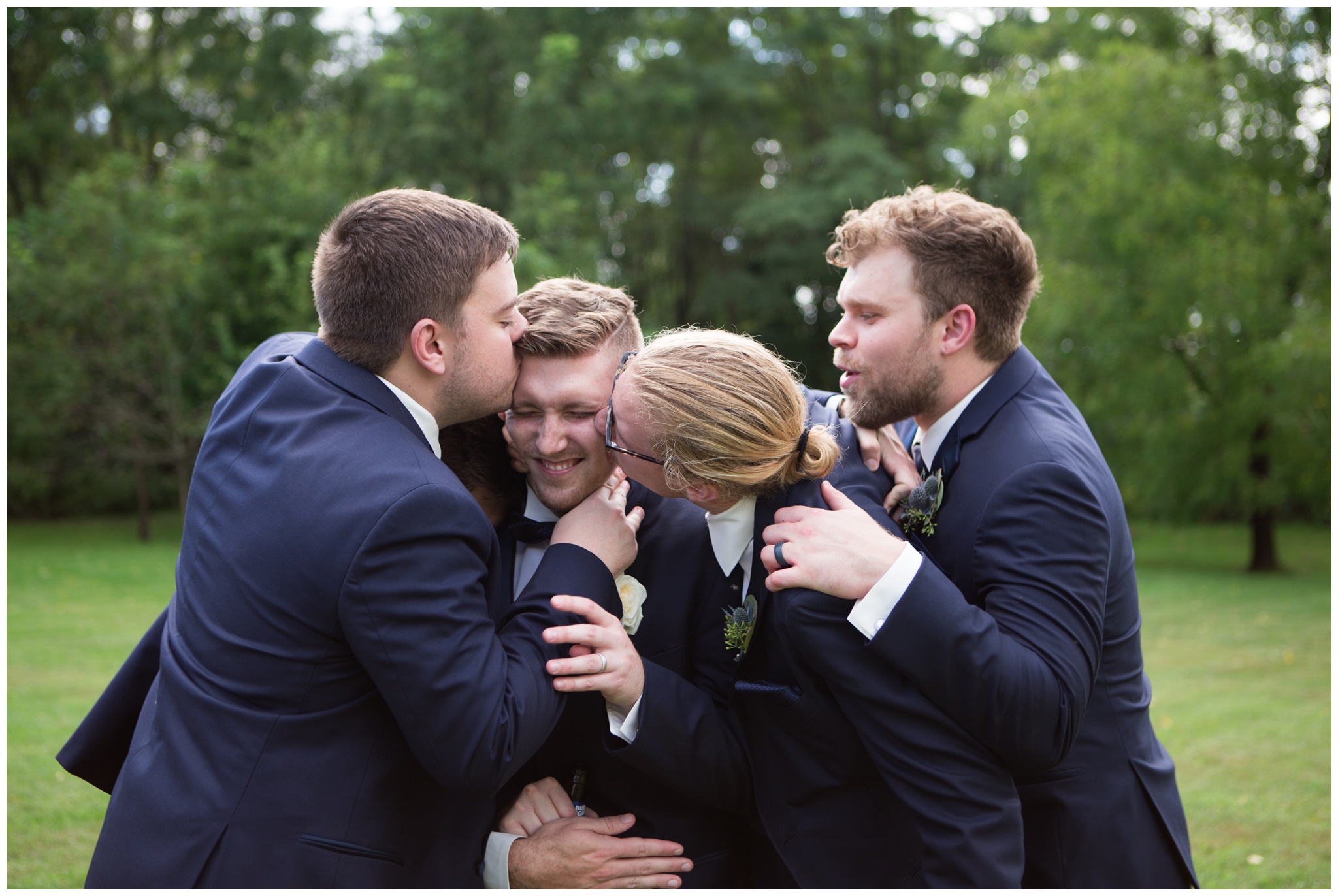 groomsmen kiss groom during portraits at the Lodge at River Valley Farm in Yorktown Indiana