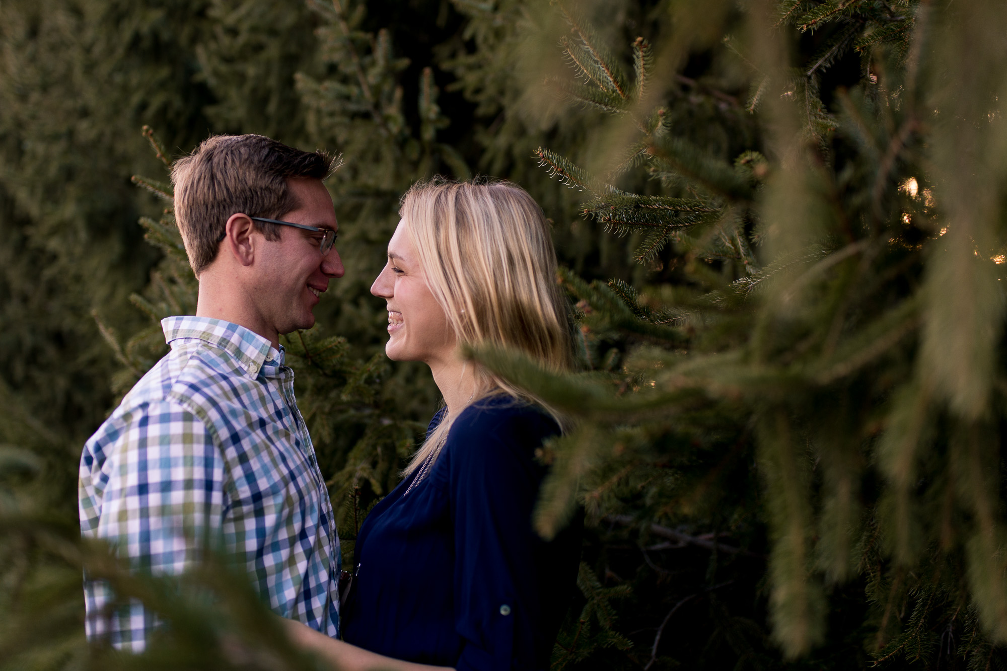 bride and groom look at each other by pinetrees during winter farm engagement session