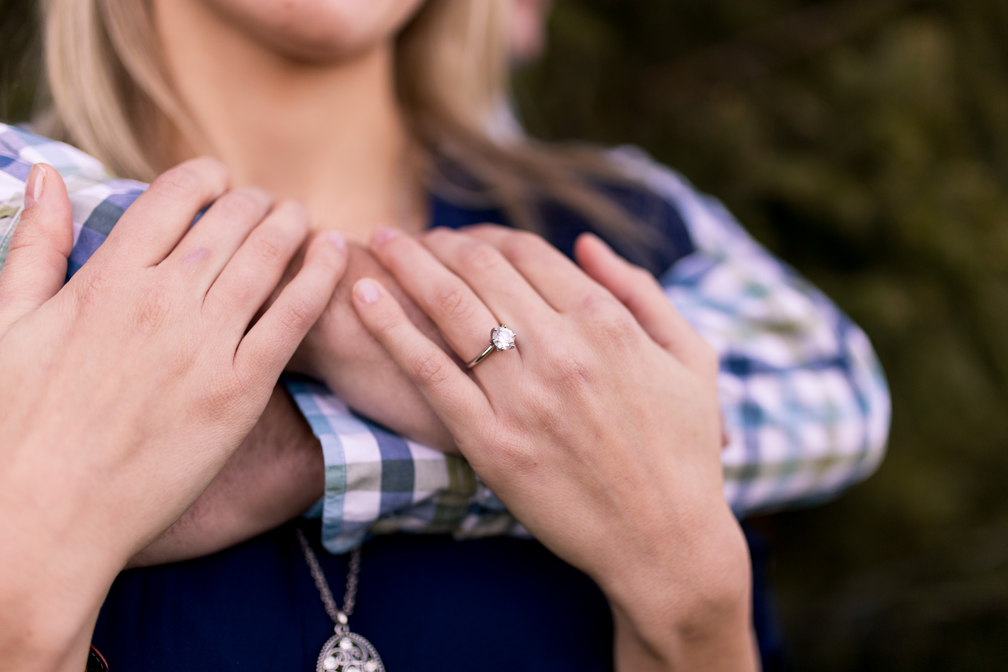 close up of engagement ring with groom's arms wrapped around bride during winter farm engagement session in Eaton Indiana