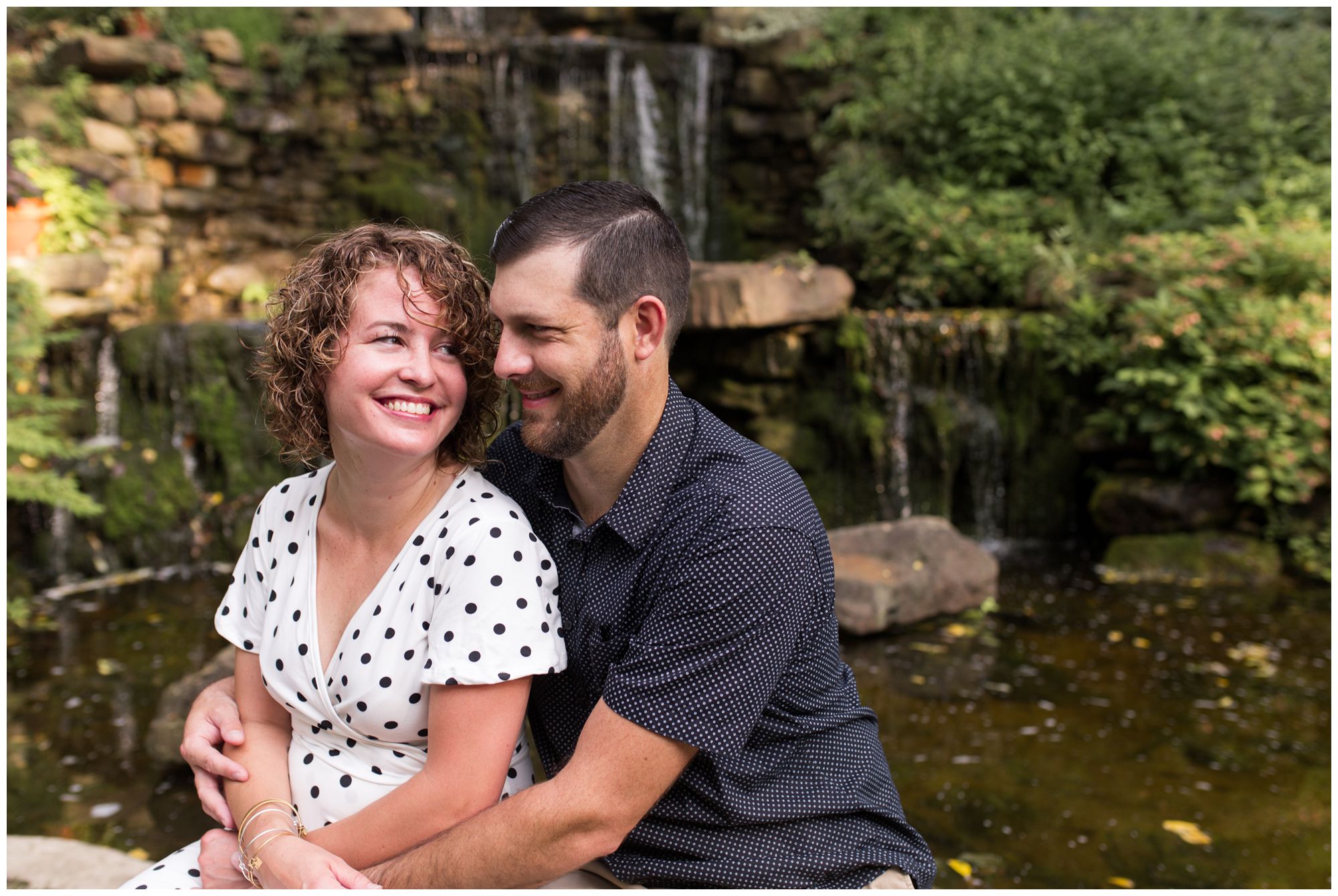 bride and groom sit in front of waterfall at Charley Creek Gardens during Wabash Indiana engagement session