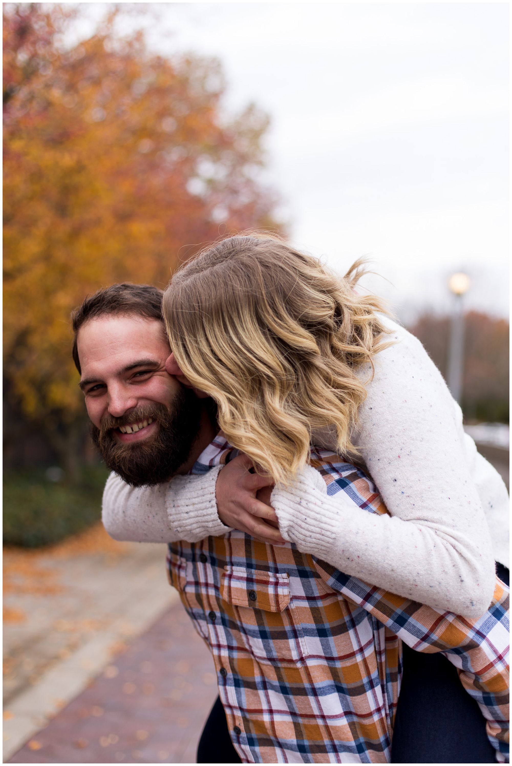 groom gives bride a piggy back ride during engagement session at Headwaters Park