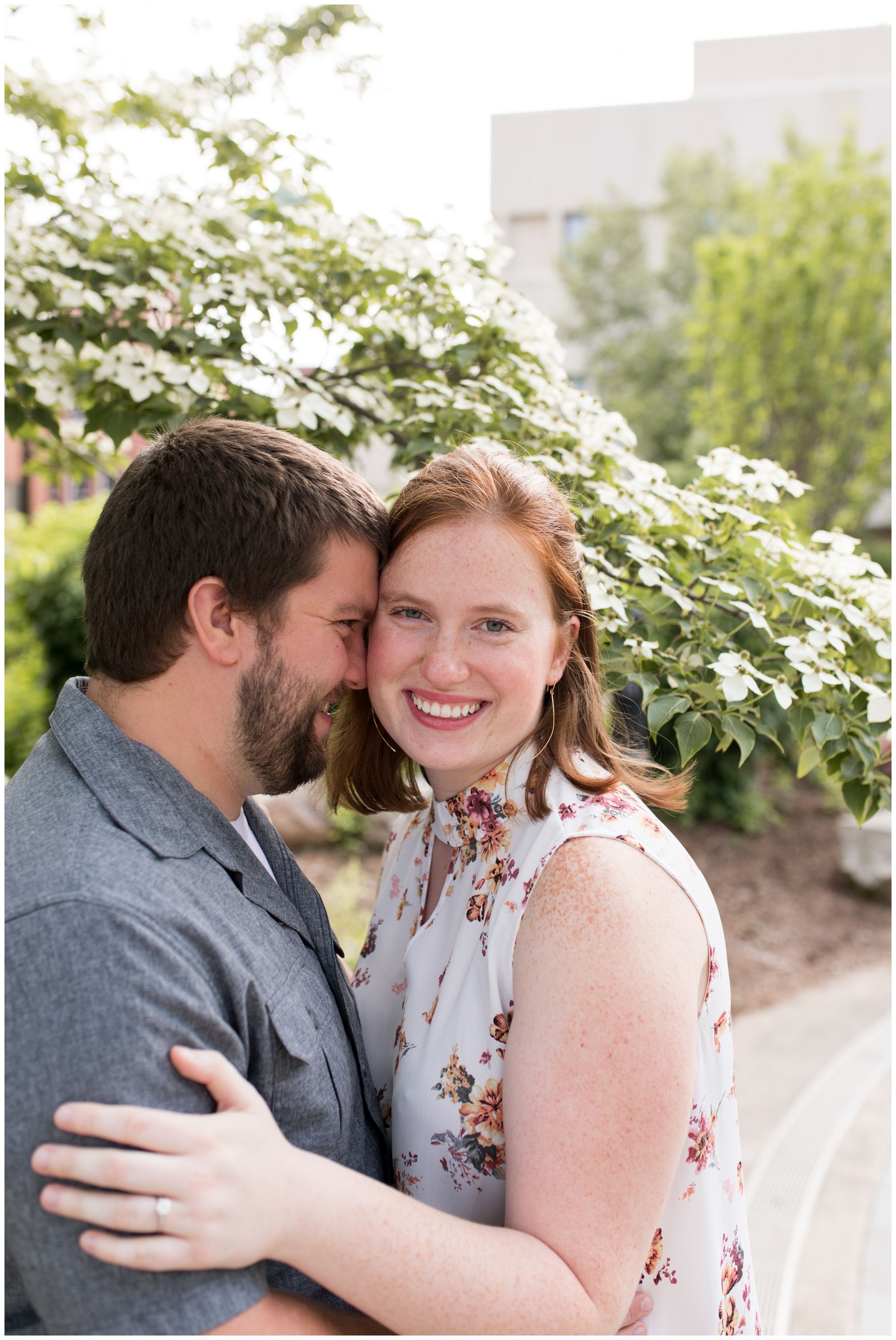 bride looks at camera while groom nuzzles side of head at Purdue University engagement session in Lafayette, Indiana