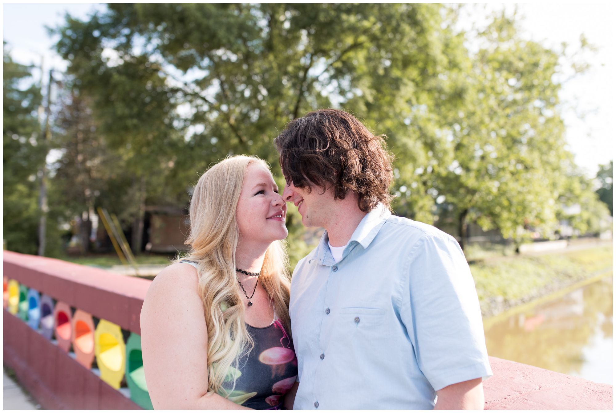bride and groom touch noses on Rainbow Bridge during engagement session at Broad Ripple