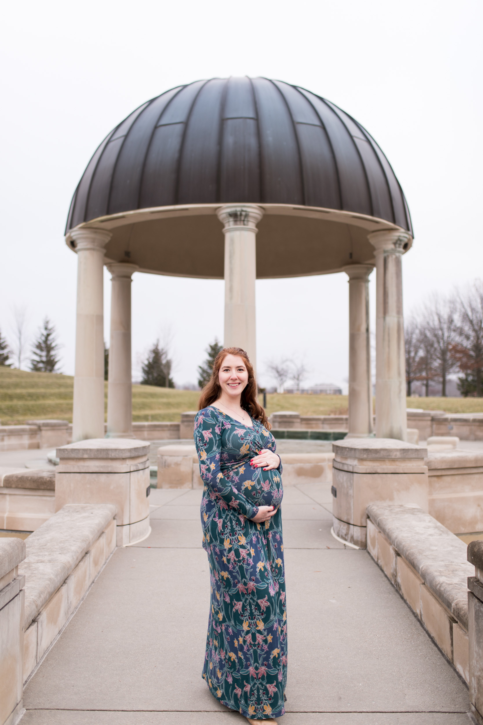 mom holds belly during maternity photos at Coxhall Gardens in Carmel Indiana