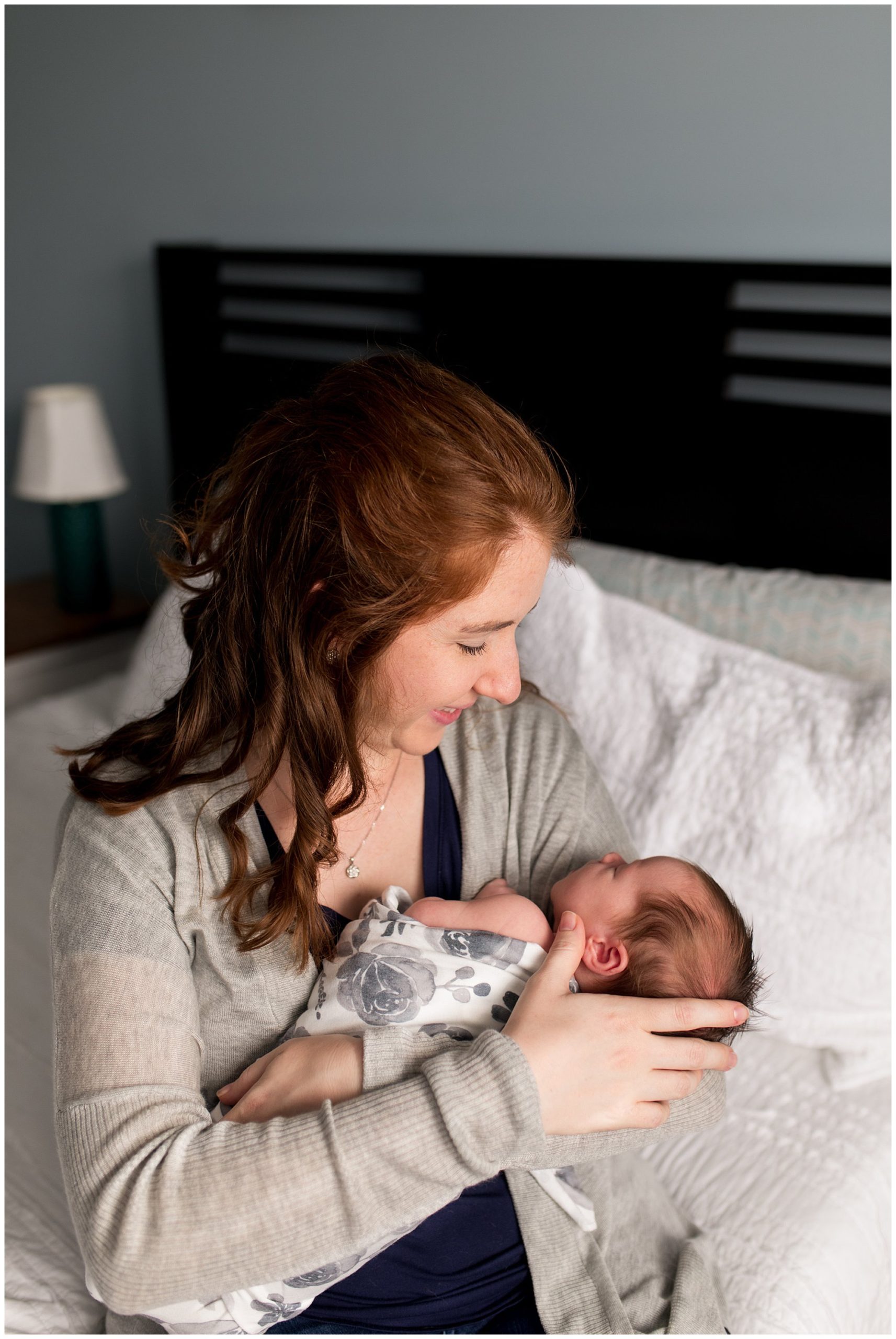mom smiles at baby in arms while sitting on bed during newborn session in Columbus Indiana
