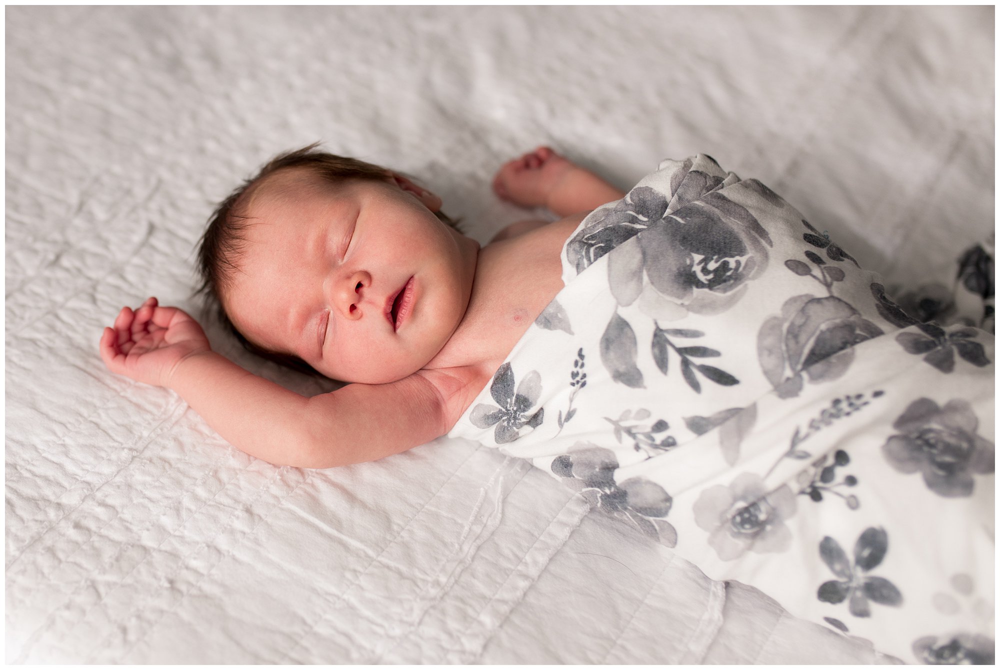 newborn baby holds arm above head in floral wrap