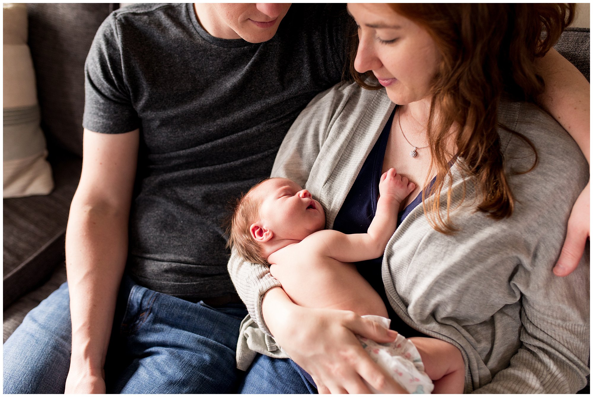 mom and dad sit on couch holding baby during newborn session in Columbus Indiana