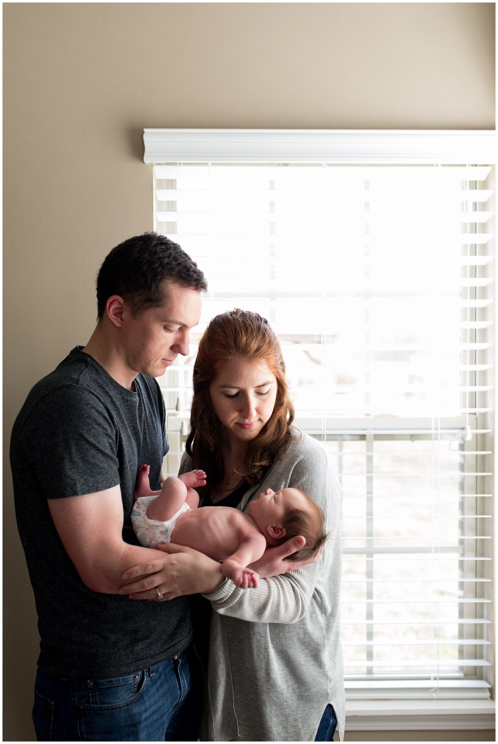 mom and dad hold baby together in front of natural light windows in Columbus Indiana