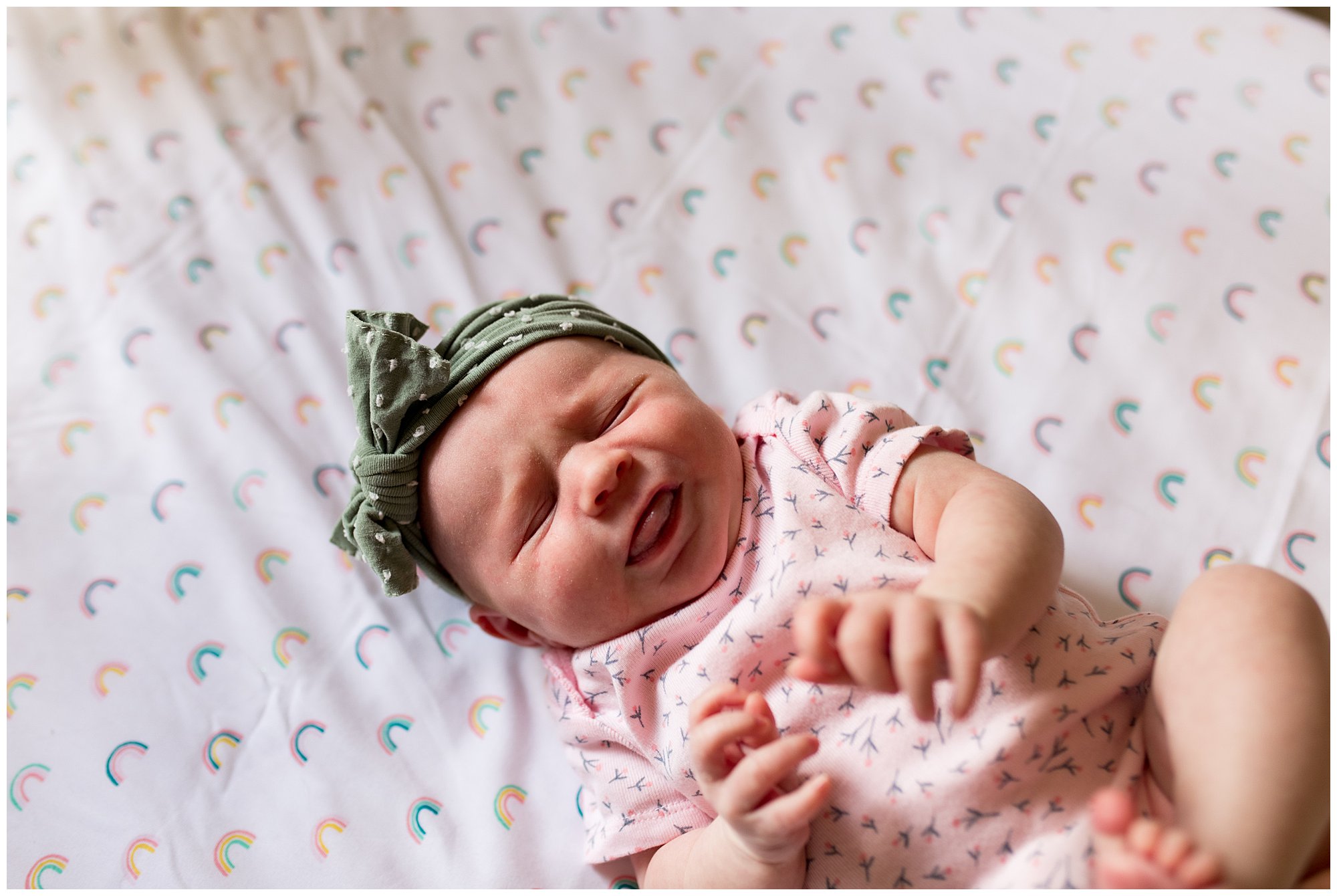 newborn lying on rainbow crib sheets with arms stretched out