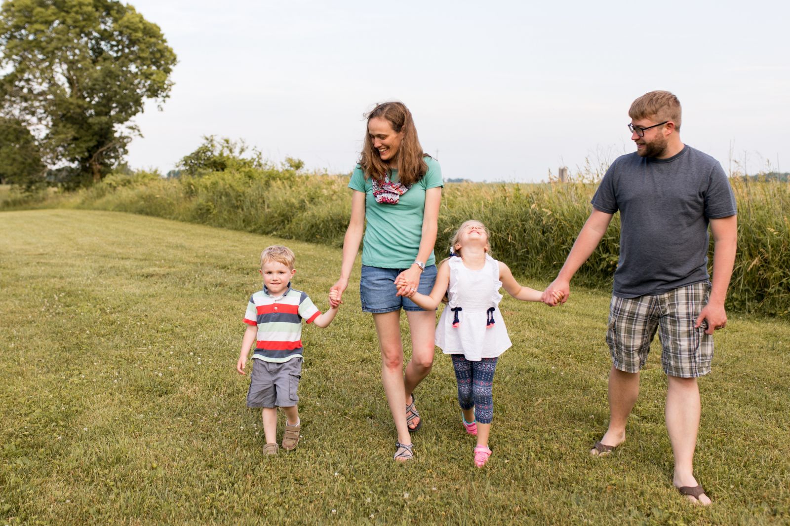 family walks hand in hand while laughing during Kokomo reservoir family session