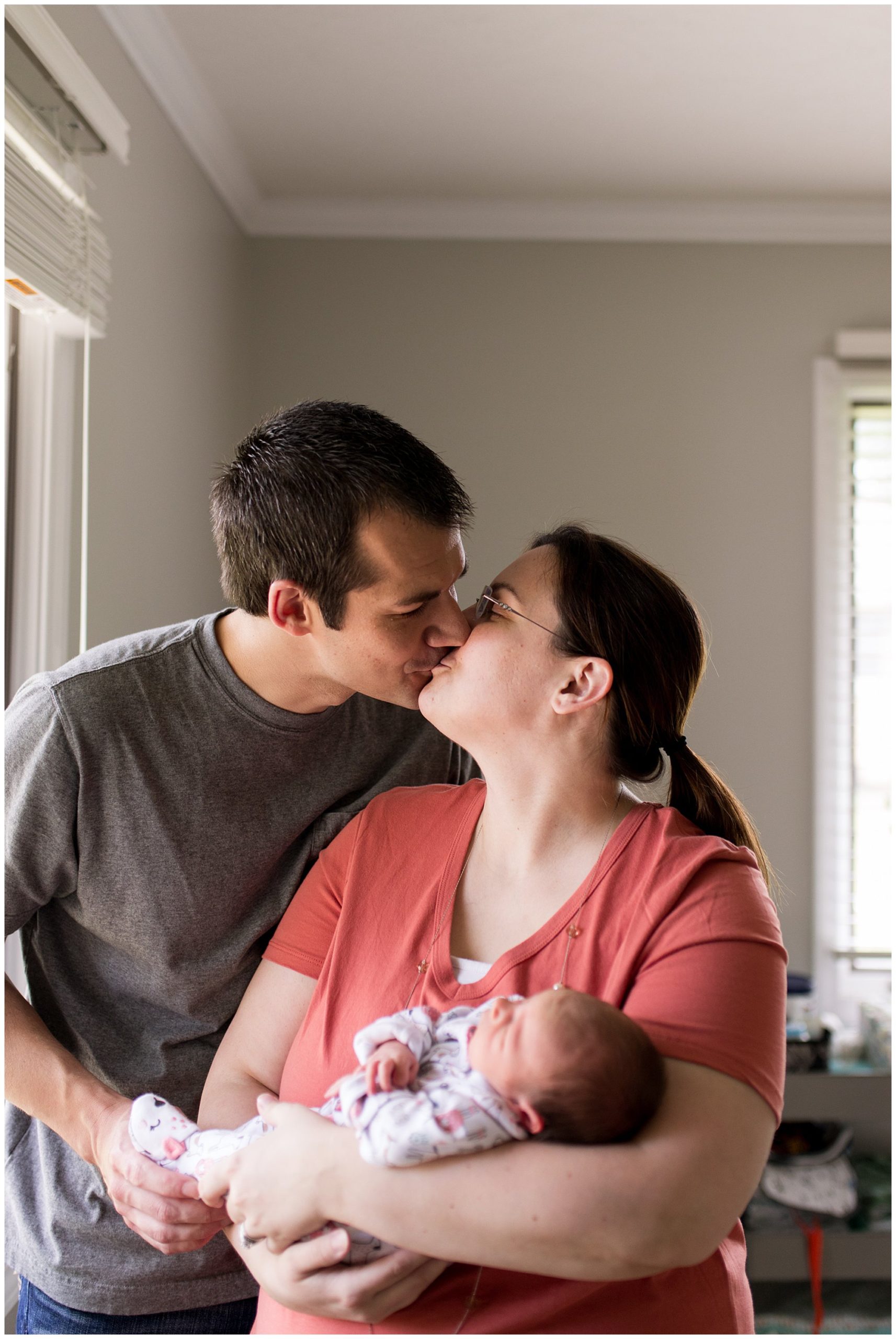 mom and dad kiss while holding baby during newborn session